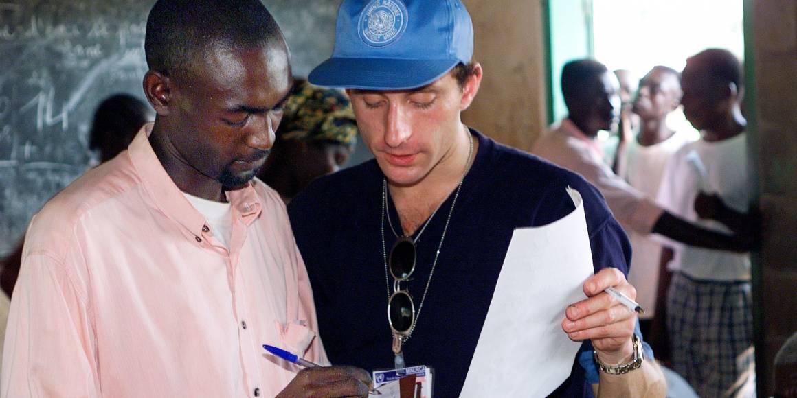 En valgobservatør fra FN hjelper en mann før han skal stemme under valget i 1998. UN Photo/Evan Schneider